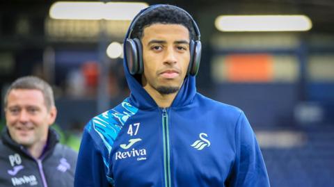 Azeem Abdulai pictured in a Swansea tracksuit, wearing headphones