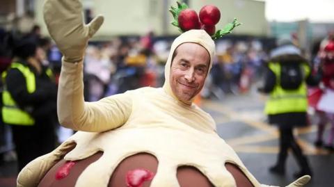 A man dressed in a Christmas pudding costume waves his hands in front of a crowd of people during last year's Christmas parade. 