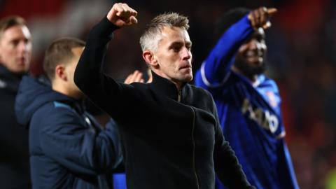 Kieran McKenna, wearing a black fleece top, punches the air in celebration after Ipswich's win at Charlton