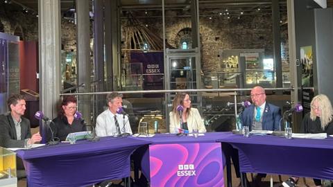 Six people sit behind desks set up inside Colchester Castle