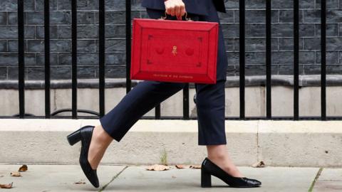 Close up view of the legs of Rachel Reeves as she walks along Downing Street. She is carrying the red box and is wearing trousers and high heels