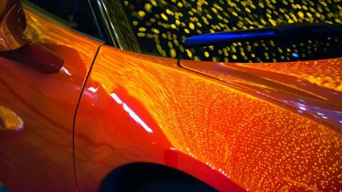 A car, showing part of its front, a door, the colour looks orange with reflections on it. 