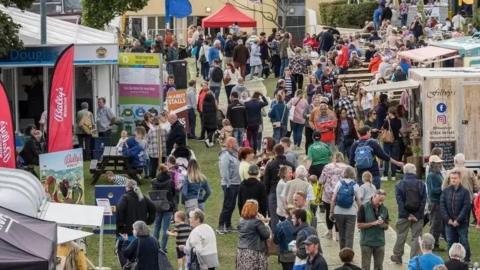 Crowds of people walking amongst food stalls in the gardens of the Villa Marina. 