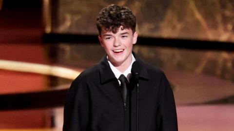 Owen standing on the stage accepting his award while smiling
