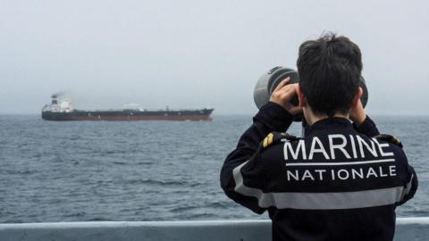 A French Navy officer wearing a black uniform labelled Marine Nationale observes an alleged Russian oil tanker sailing in the Atlantic ocean.