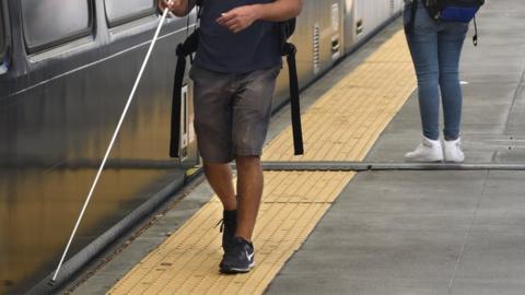 Visually impaired person with a stick next to a train