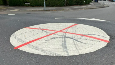Image shows a mini-roundabout that has been painted white, with a red cross on it, to give it a likeness to the flag of St George, the national flag of England