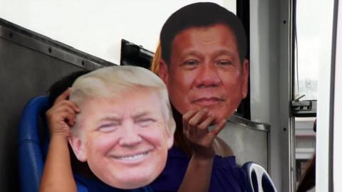 Two people hold up masks of Trump and Duterte