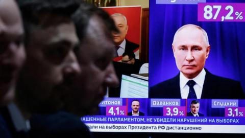 Men sit near a TV broadcasting news on the results of Russian incumbent President and presidential candidate Vladimir Putin, on the final day of the presidential election in Moscow,