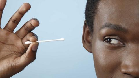 Close up of a young man holding cotton bud and pointing it towards his ear.