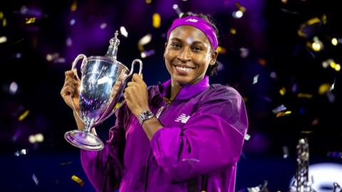 Coco Gauff smiles and holds up the Billie Jean King Trophy