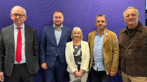 Five candidates, four men and one woman, stand in front of a purple BBC radio studio background.