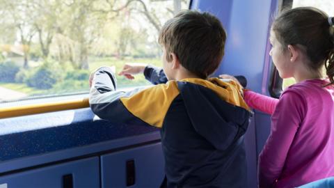 A boy and a girl look out the front window on the top level of a bus