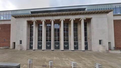 A large grey stone and brick building with pillars in the centre. University of Wolverhampton at The Halls is written above the entrance.