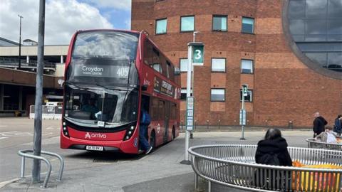 A red double decker bus in a town centre. 