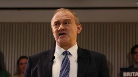 Sir Ed Davey in a blue tie and suit delivering his speech 