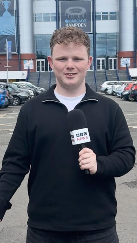 Ryley Bowman - young man in a dark jumper, holding a BBC news microphone, standing in front of Hampden stadium