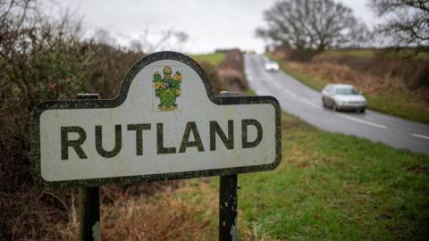 Rutland sign on a road leading into the county with cars travelling along it