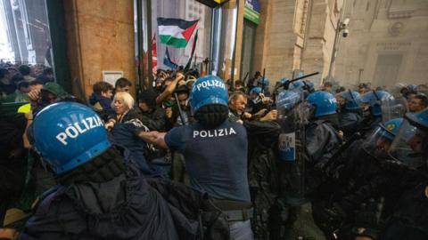 Police wearing blue riot helmets clash with protesters in Milan's central station. 