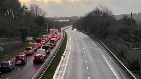 A long queue of standstill traffic on a dual carriageway. The carriageway in the opposite direction is empty.