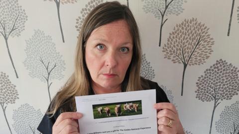 Women with long hair. She's looking sad to the camera. She's holding an A4 paper document with a voucher with dogs running around 