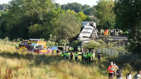 A group of people stood next to a derailed train.
