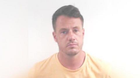 A mugshot of Cameron Ross, looking straight at the camera wearing a yellow t-shirt against a white background.