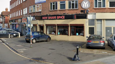 A general view of New Shahi Spice, a restaurant on the ground floor of a third-storey building, with a car parked outside it.