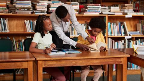 Two children look at books in library with an adult.