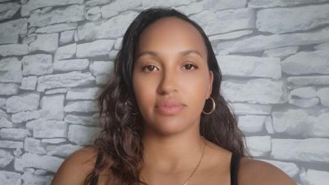 Image of Charlene, a young woman with dark hair and eyes and gold hoop earrings in front of a grey patterned wall