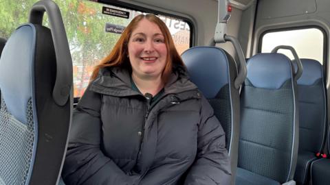 A woman wearing a black jacket, sat down on a bus.