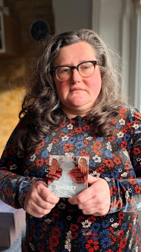 A woman in a flower dress holds a picture of her babies hands.