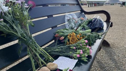 Bouquets of flowers on a bench with a hand-written note.
