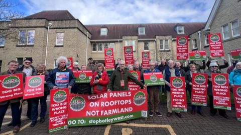 Protesters from the Stop Botley West group outside West Oxfordshire District Council's headquarters holding signs, most of which say: "Too big! Wrong place. Protect our heritage." 