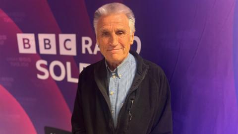 Bob Lakin a grey haired man stood in front of a purple BBC Radio Solent backdrop