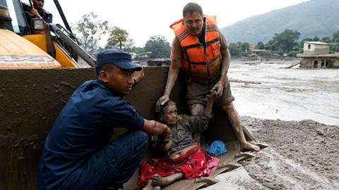 Rescuers transport an elderly woman on heavy machinery amidst flash floods