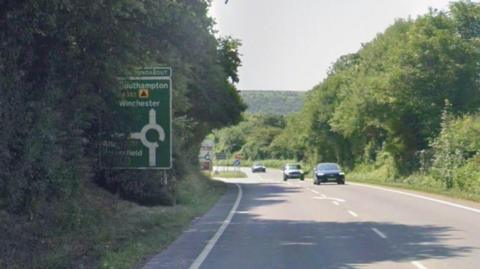 A view of Spitfire Link Road in Winchester on a sunny day. There are a few cards driving on the road. There is a road sign for Southampton and Winchester.