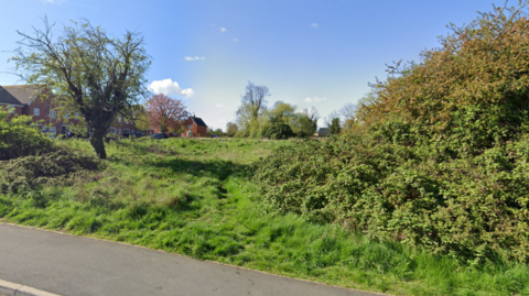 unused patch of land with new houses in the distance