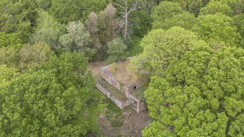 An aerial view of the old brick power station surrounded by green woodlands