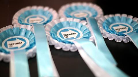 A close-up of five Reform UK election rosettes in turquoise blue and white colours.