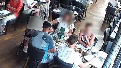 CCTV image showing a group of people sat at a dining table.