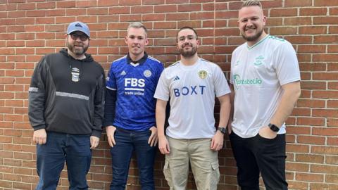 Four football fans, wearing their team's merchandise in front of a brick wall