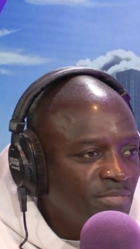 Akon is sat with headphones on. He is speaking into a purple microphone.