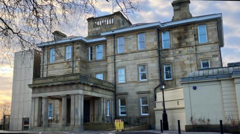 Large light-stone brick mansion set across the background of a blue morning sky.