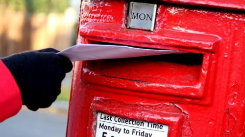 Man posting a letter in red postbox
