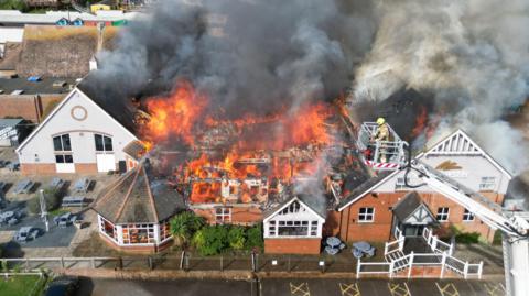 A Harvester building on fire. There is a aerial ladder platform in the foreground.