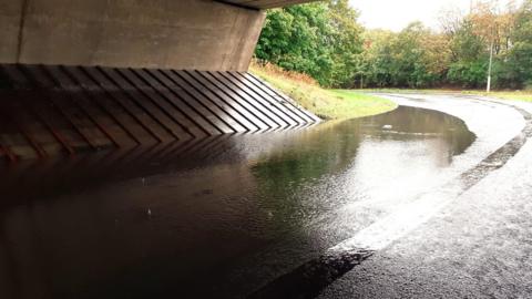 A flooded road that runs beneath a bridge. 