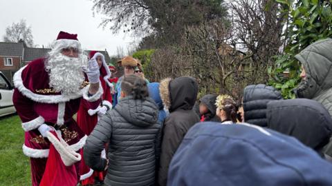 Father Christmas hands out presents to a small group of school children stood outside