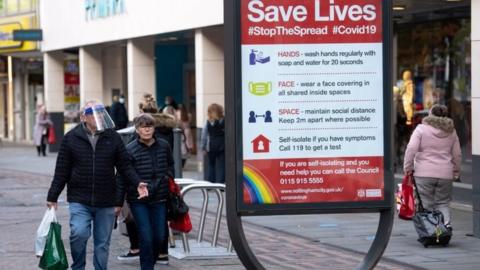 A man wearing a face shield walks past a coronavirus advice sign in Nottingham city centre