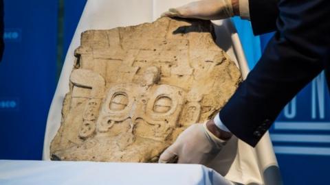 Unesco staff members place the Mayan stela on a display before the handover ceremony